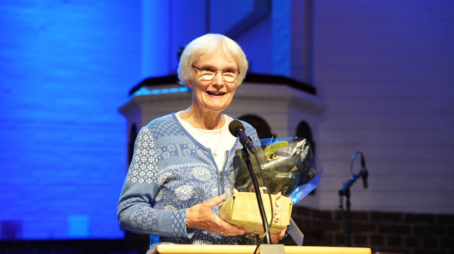 Eldre dame tar i mot pris og har en takketale i en kirke. Foto.