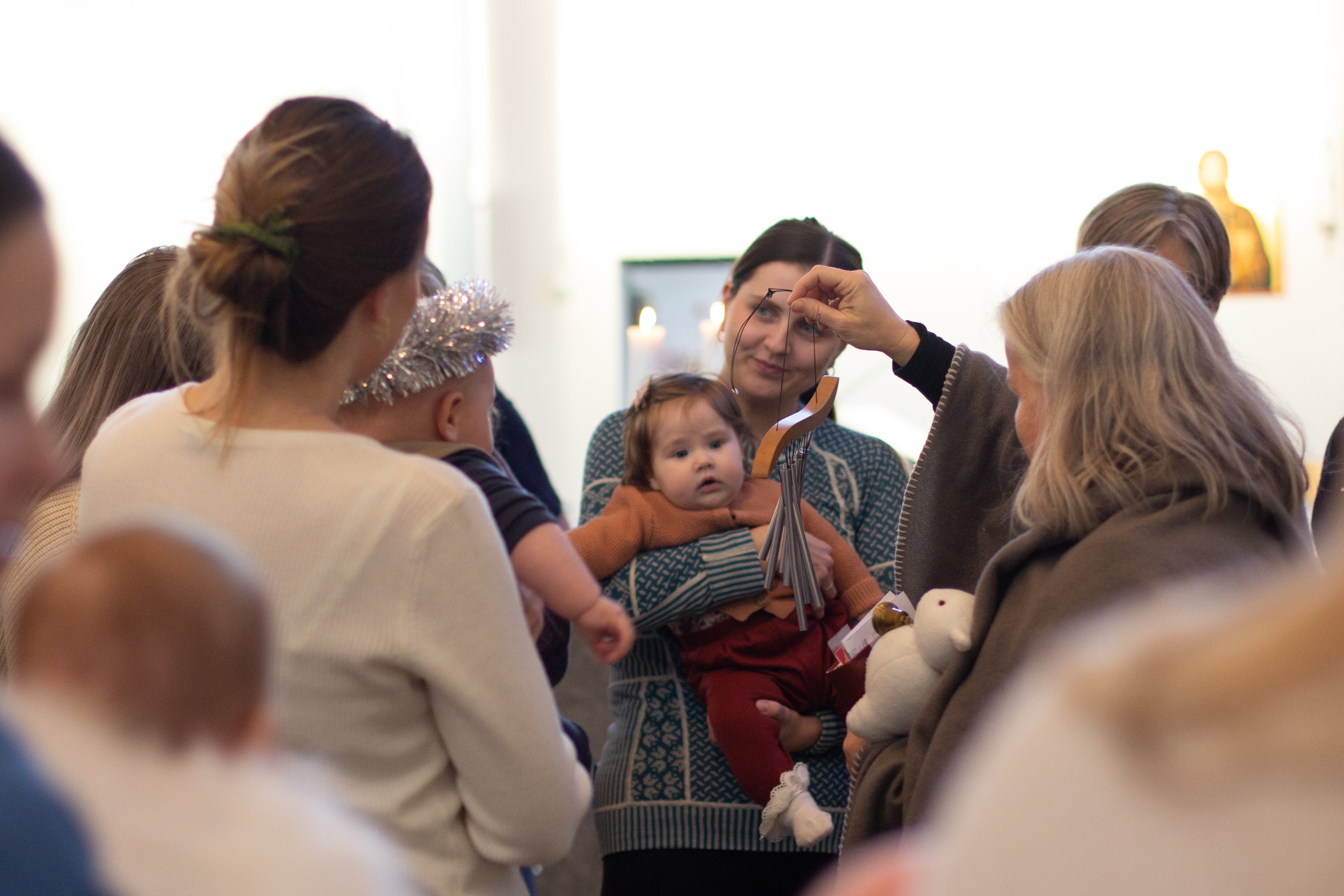 En dame holder opp et lite klokkespill og viser til babyene som ser på