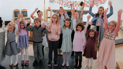 Fleire barn står oppstilt framme i Sund kyrkje med hendene opp